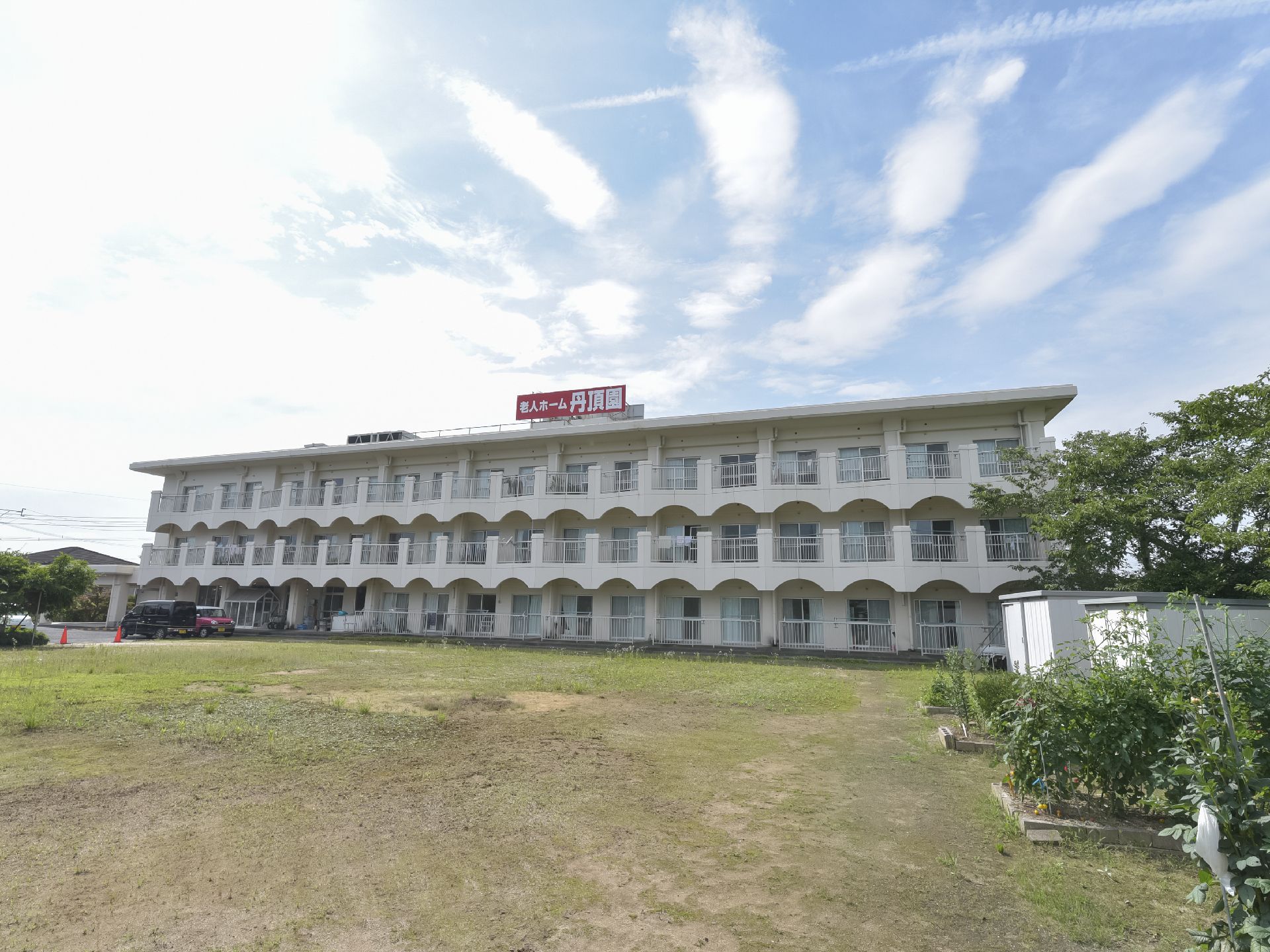 田畑に囲まれた建物は白を基調とした３階建て。周辺には木もたくさん植えられている。