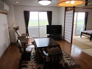 障子で区切られ、奥には畳敷きの和室があり、手前にはフローリングの部屋があり、テレビやテーブルセットがある。