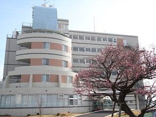 白を基調とした大きな建物は日当たりのいい場所に建っている。手前には桃の花が咲く木がある。