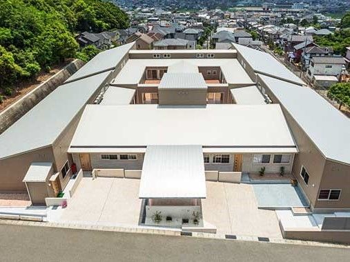 平屋建ての建物を空中から見下ろした様子。左側には山があり、奥には住宅地が見える。