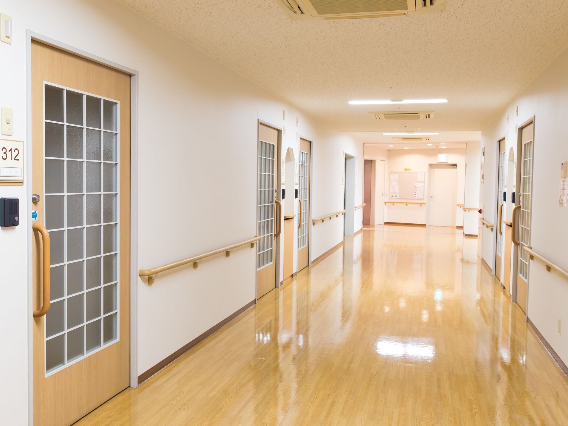 空調と照明の付いた明るい内廊下が続いている。手すりの設置された壁には、白い格子とすりガラスの扉が並んでいる。