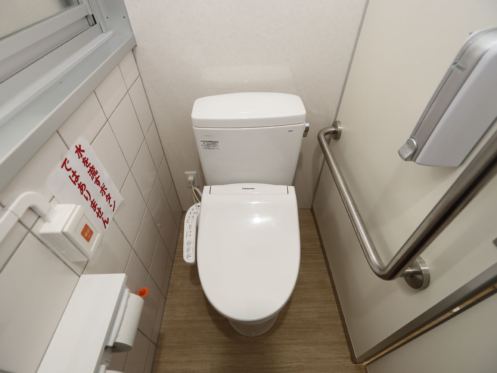 バリアフリー完備で周囲に手すりが設置された便座、洗面台があるトイレ