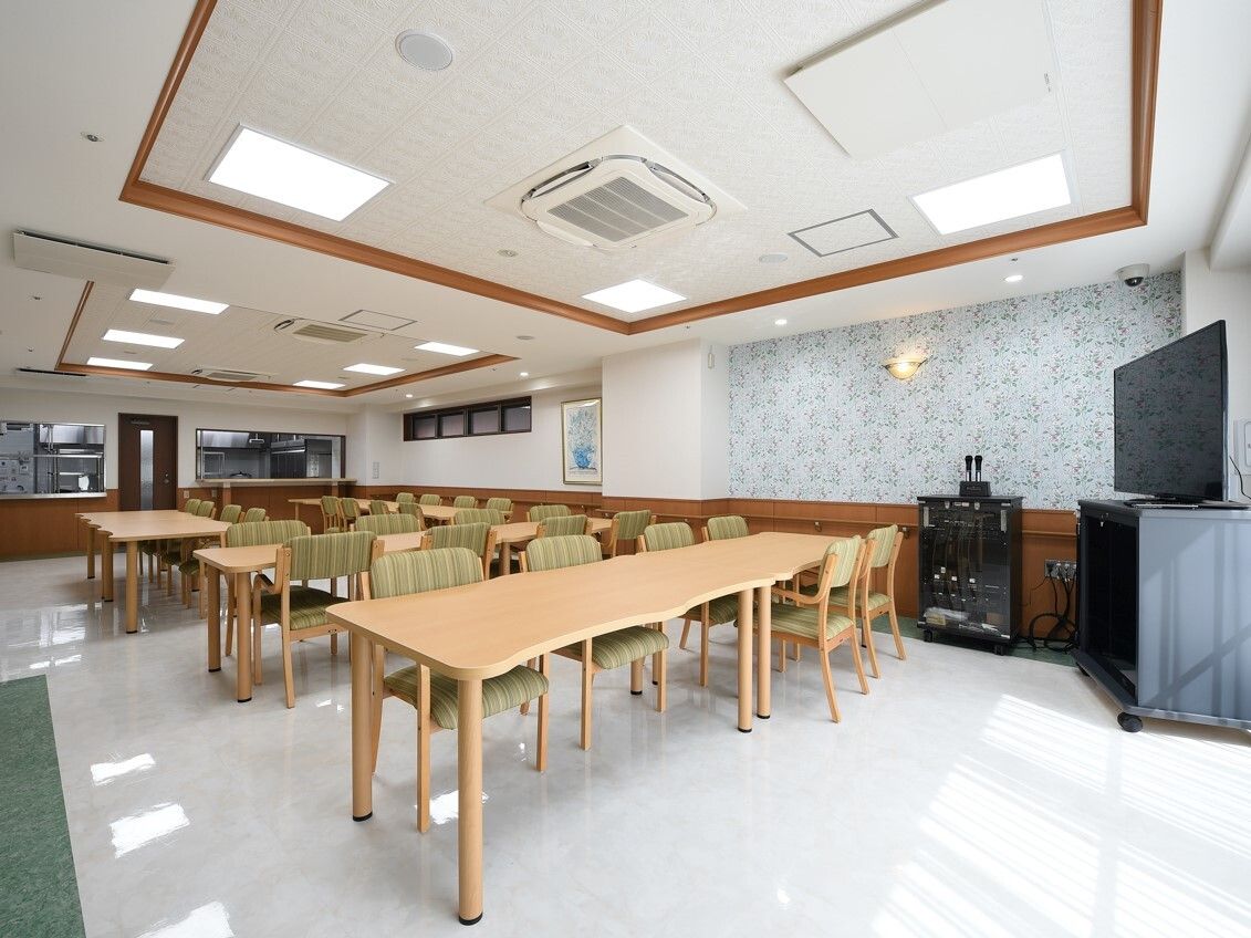 木製のダイニングテーブルセットが複数置かれ、大きなテレビが設置された食堂には厨房もある。