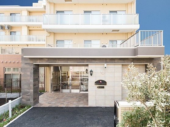 各フロアにベランダがあり、日当たりのいい場所に建っているベージュの外壁の建物。草木も植えられている。