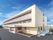 各フロアにベランダがある3階建ての建物はベージュ系の外壁。周辺には住宅地もある。