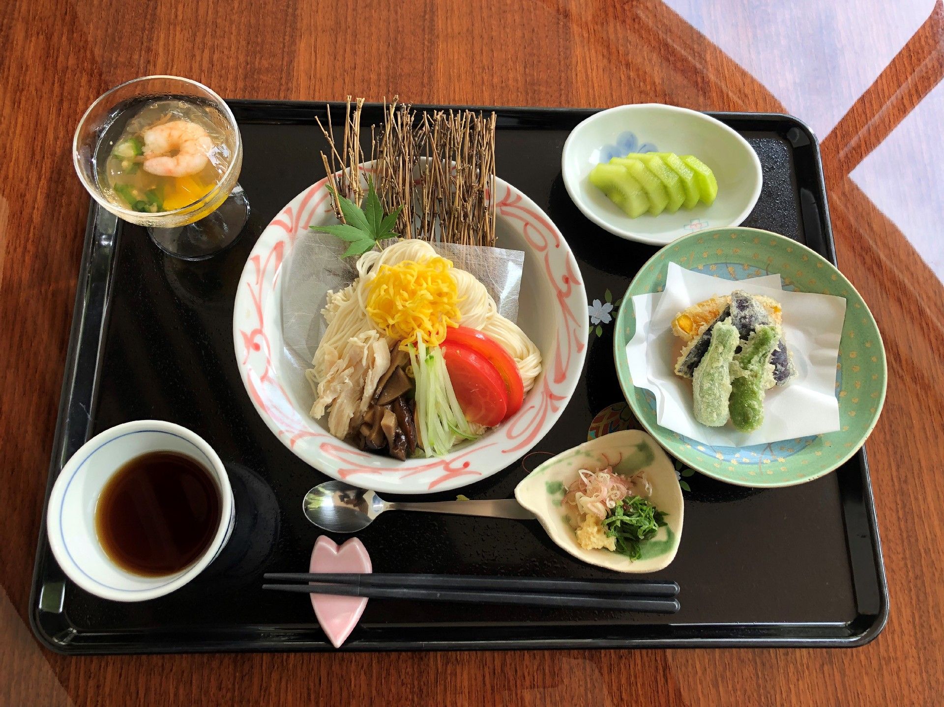 黒い盆の上にてんぷらやエビのゼリー寄せ、キウイ、具が添えられたそうめんなどが乗っている。