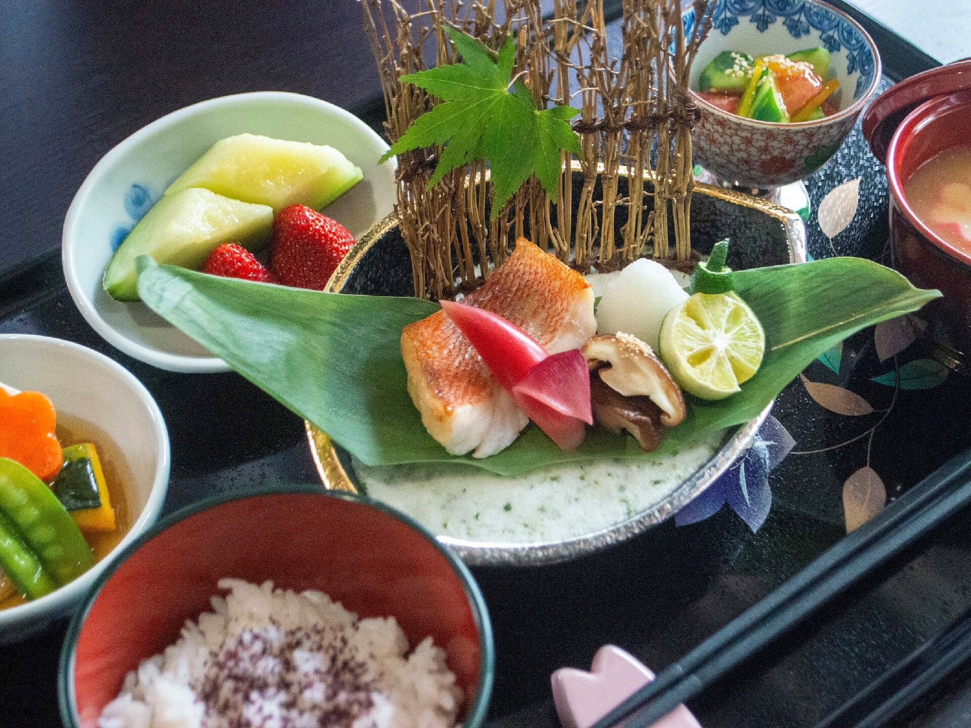 赤魚の焼き魚や煮物、季節のフルーツなどが並べられた食事の一例