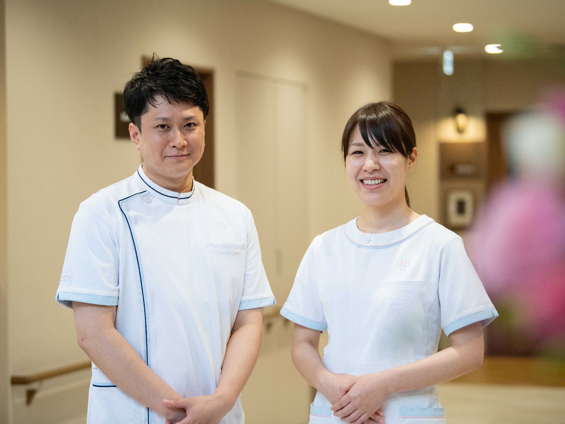 ナース着を着た男女スタッフの写真、前で手を組んでにこやかな表情をしている
