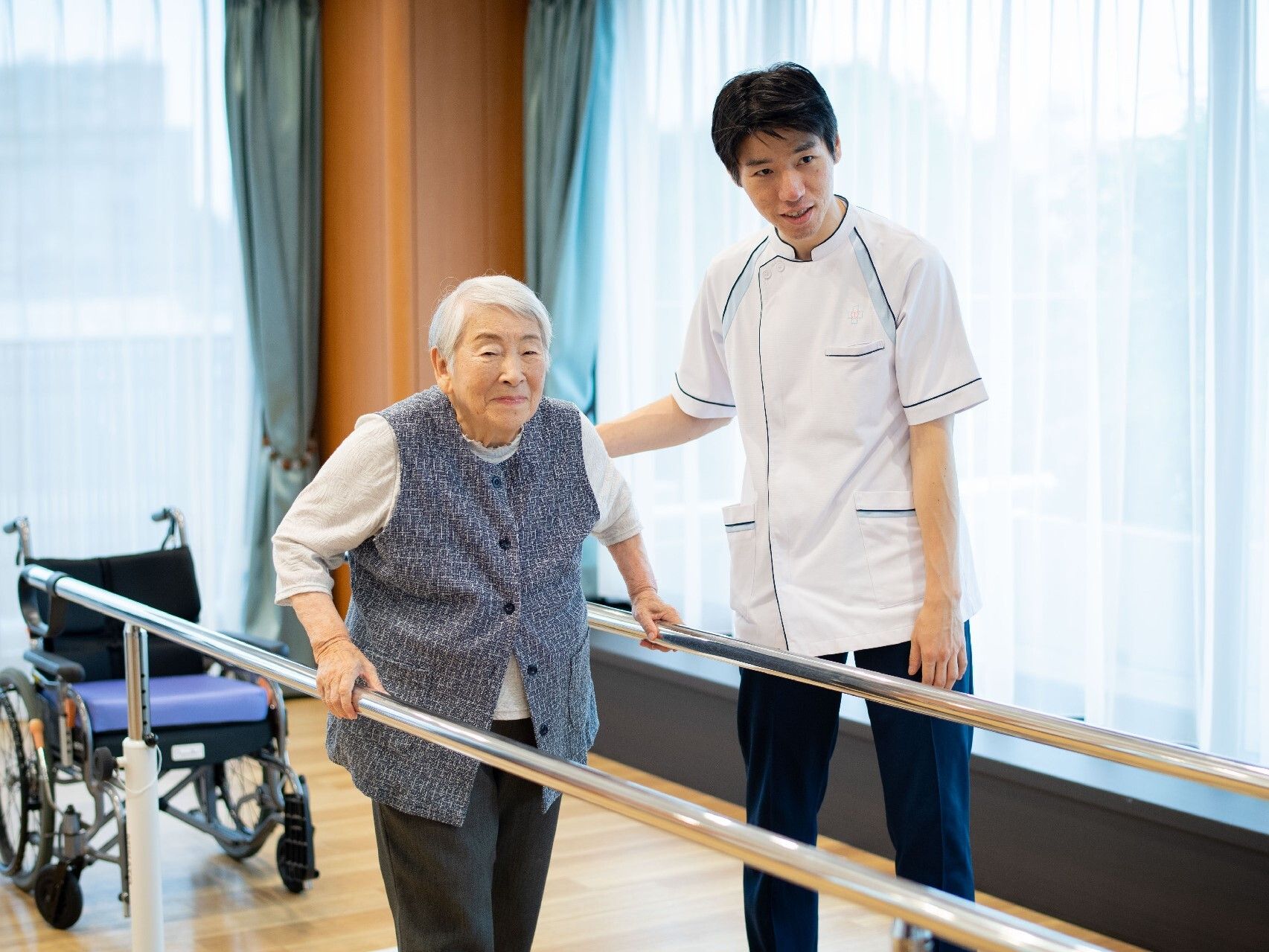 歩行器を使いながら歩行訓練している施設の高齢者の様子。専門家が付き添っている