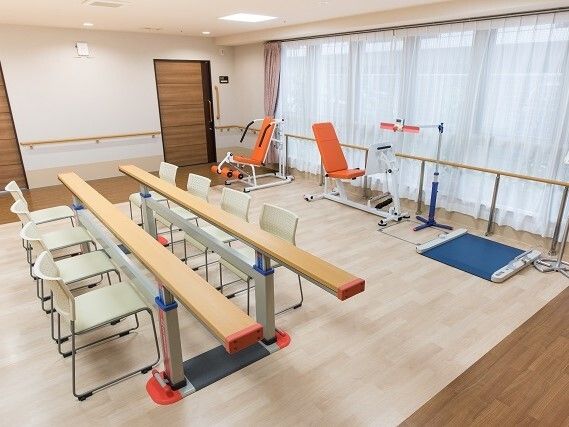 リハビリマシンや平行棒が設置されているリハビリスペース。平行棒の周りにはたくさんの椅子が置かれている。