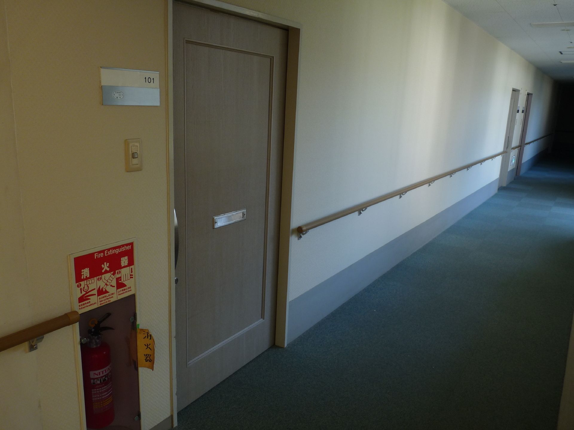手すりがついた施設内の廊下と個室のドアの様子。施設内の共有スペースの写真