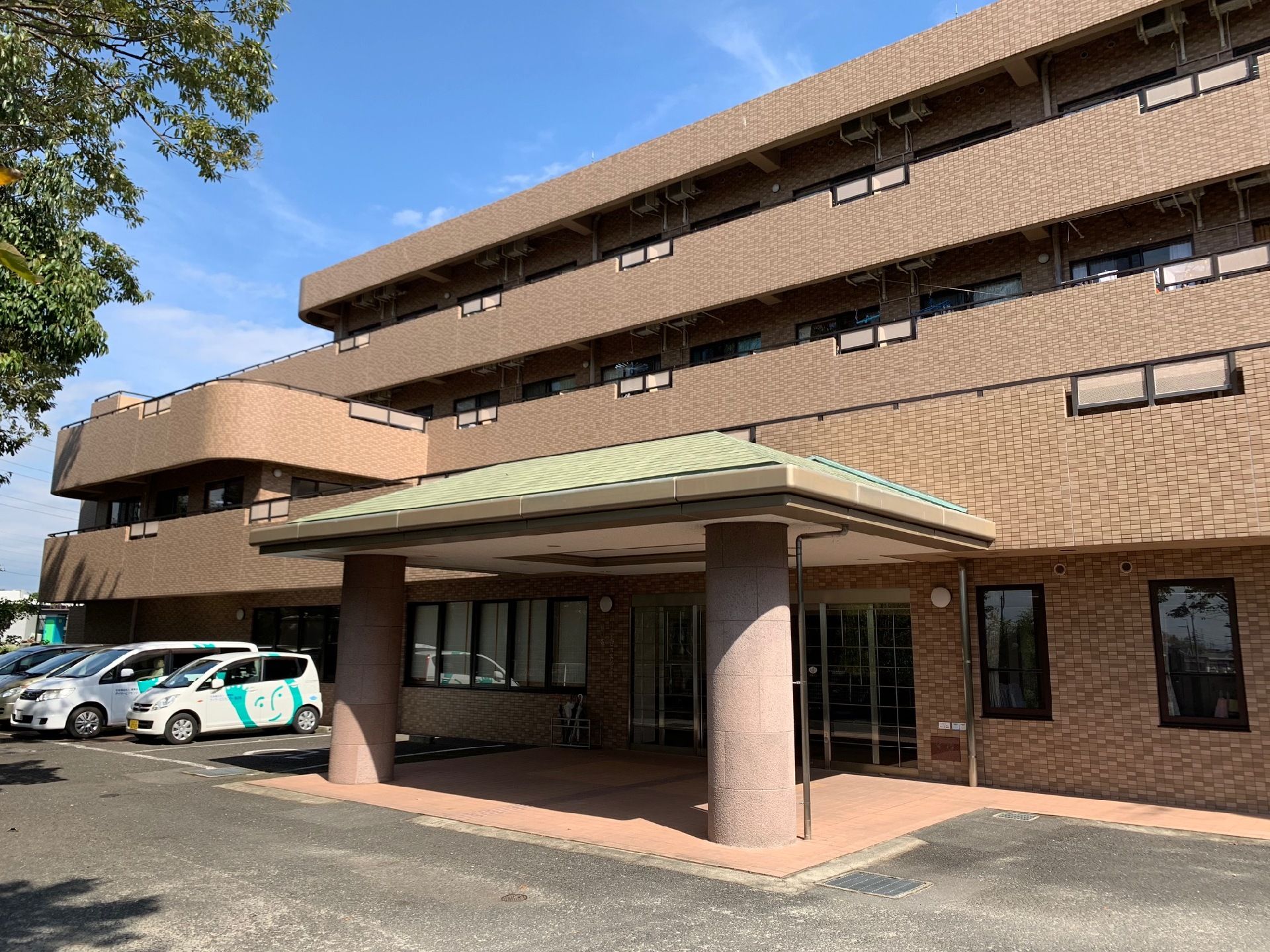ブラウンを基調とした外観。玄関先には屋根が付き、建物前には駐車スペースがある。