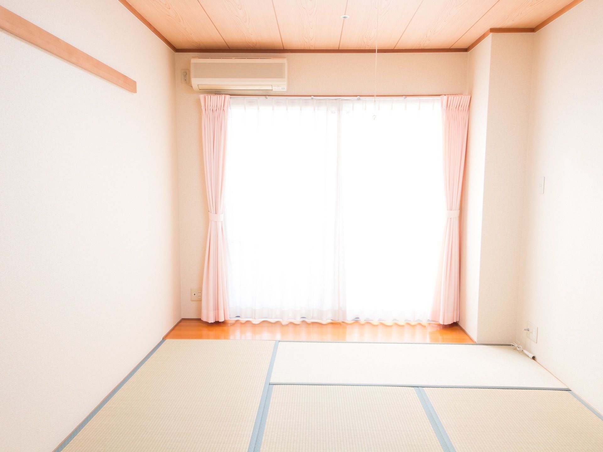 和室タイプの居室である。部屋の奥には外へ出られる大きな窓があり、カーテンが下がっている。窓の上にエアコンが設置されている。