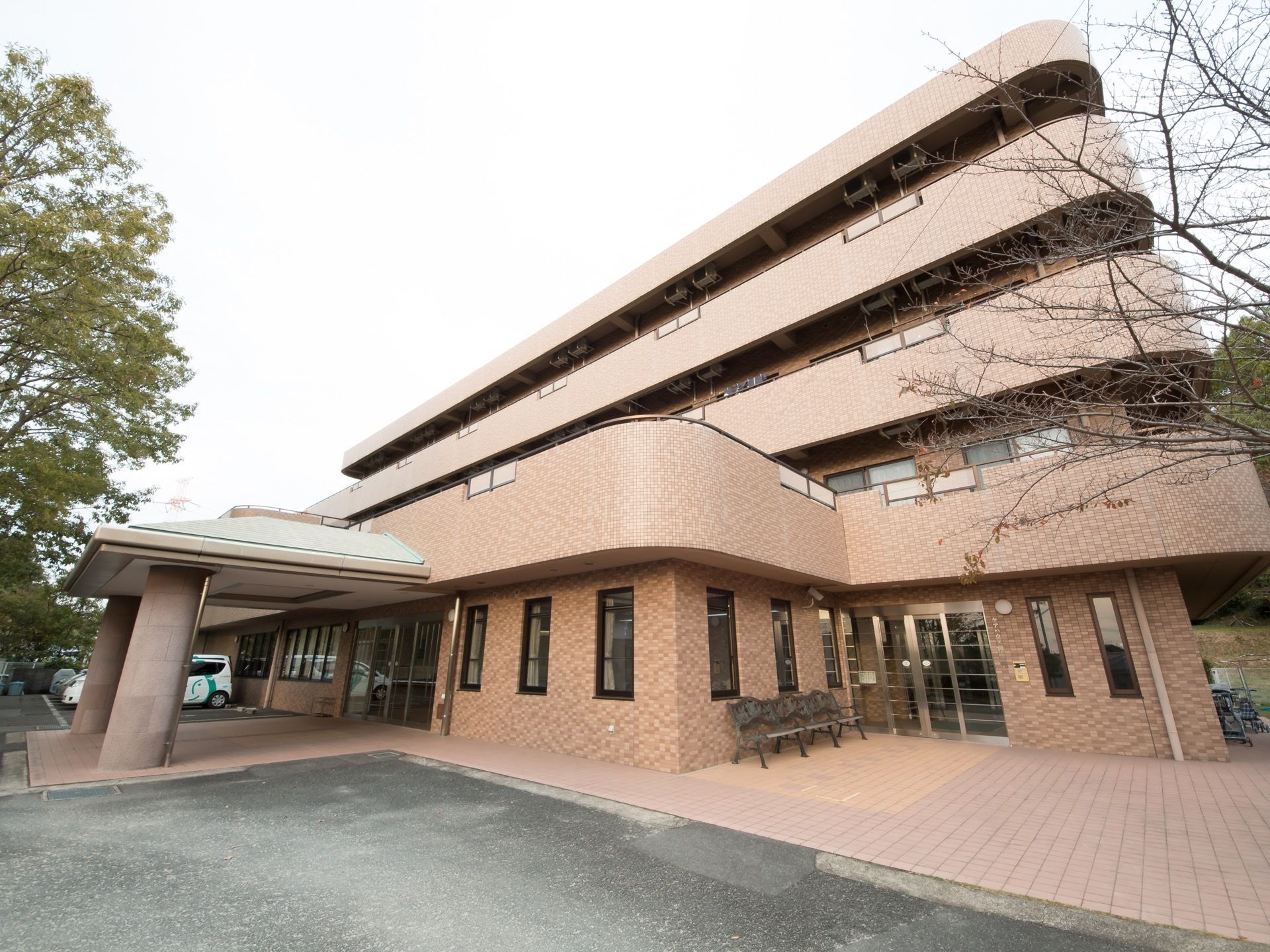 茶色の外壁の３階建ての建物で、建物の角はカーブを描いている。入口は自動扉で、玄関前にベンチが置かれている。