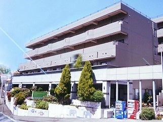 グレーの４階建ての建物。周辺には緑が多く、自動販売機も２台ある。