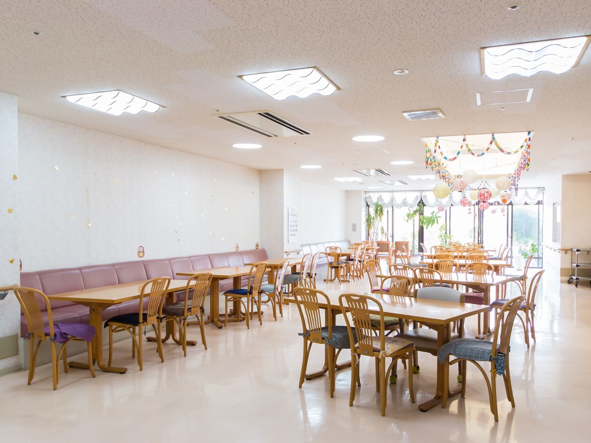 複数のダイニングテーブルが配置された、広い食堂である。壁側にはパープルで統一されたソファが備えつけられている。