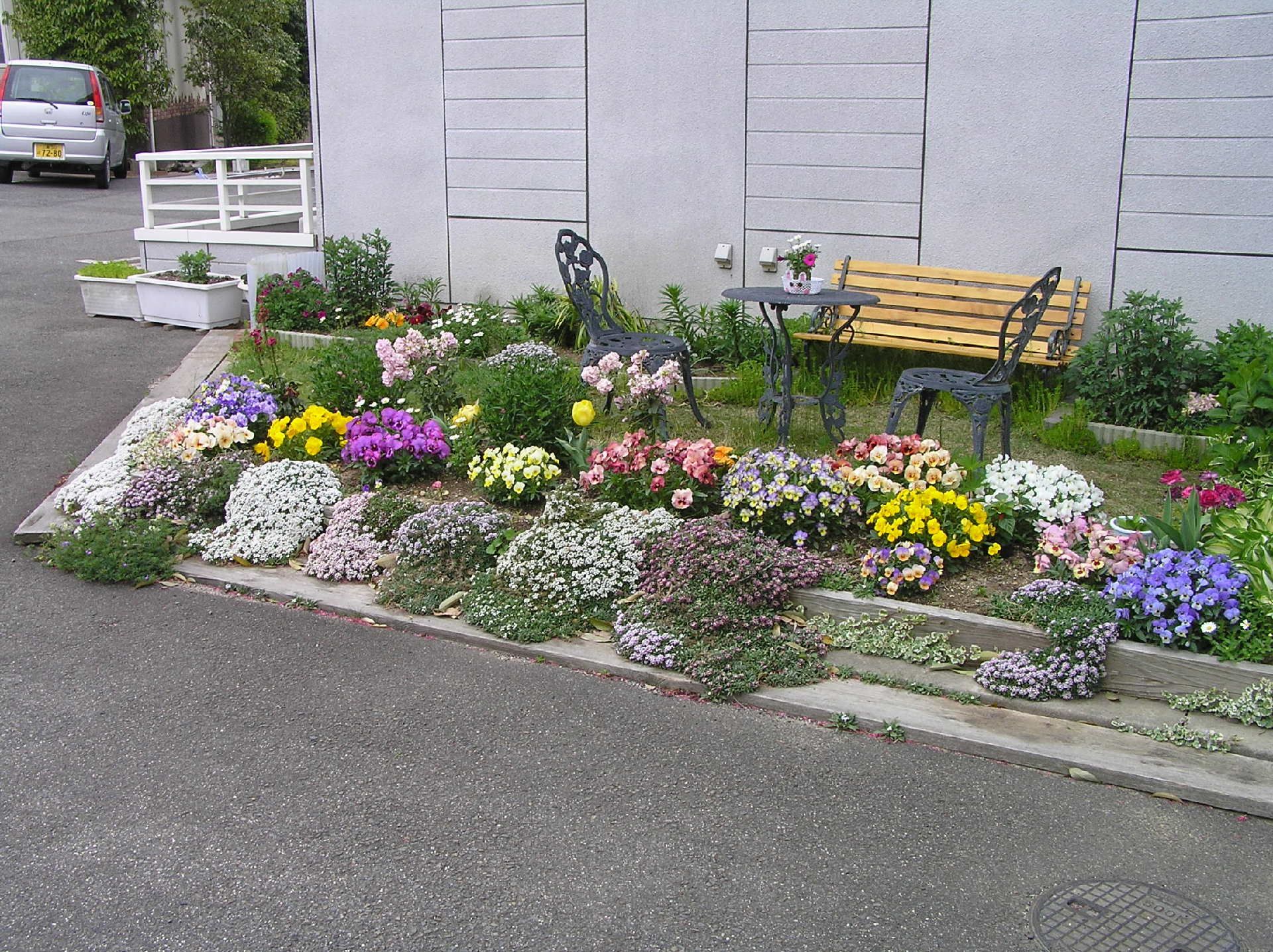 黄色紫、ピンクといった色とりどりの花が咲いた庭。ベンチなども置かれている。