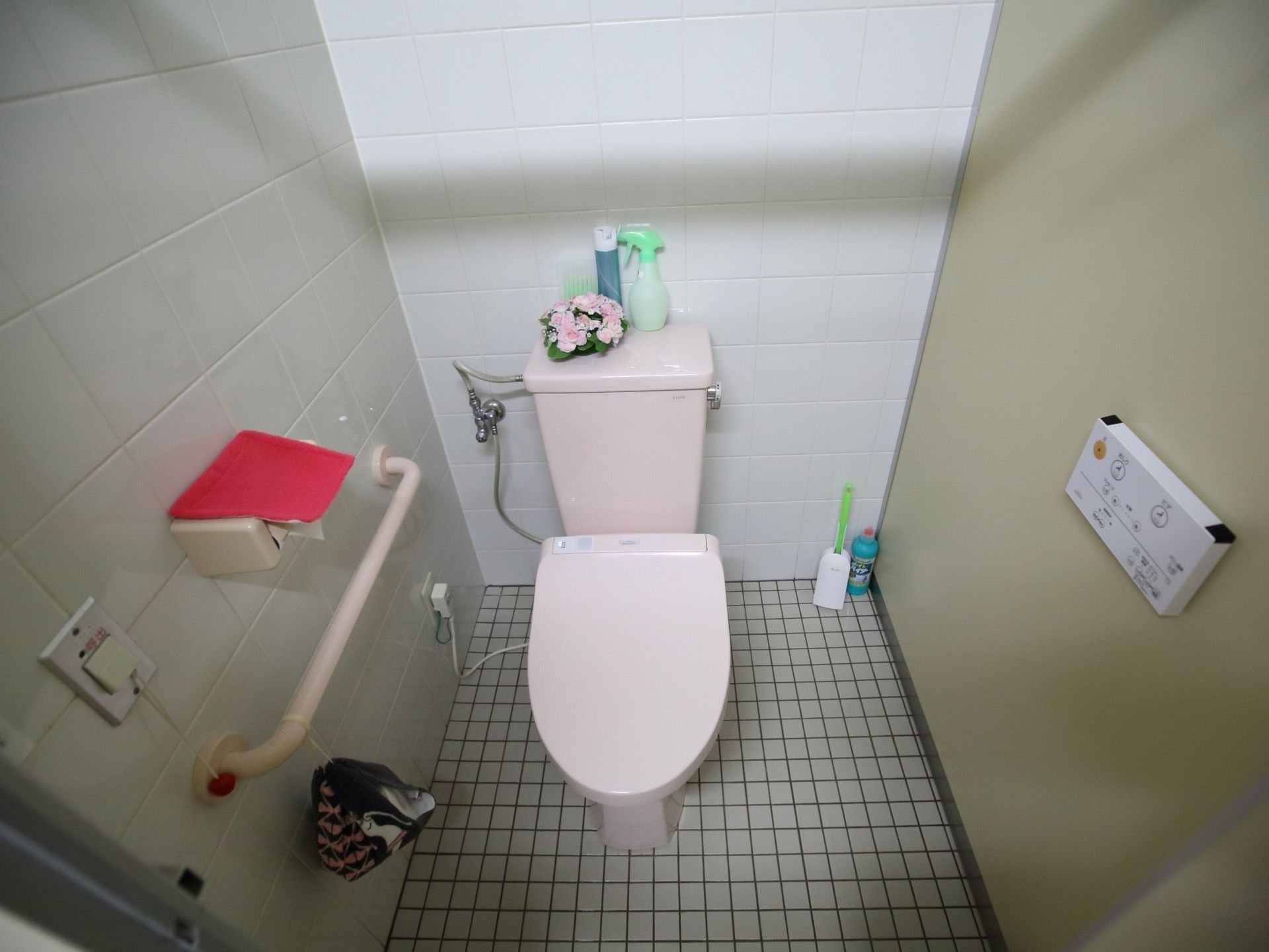 壁に手すりと緊急呼び出しブザーが設置されているトイレである。温水洗浄便座器が完備され、清掃用具が配備されている。