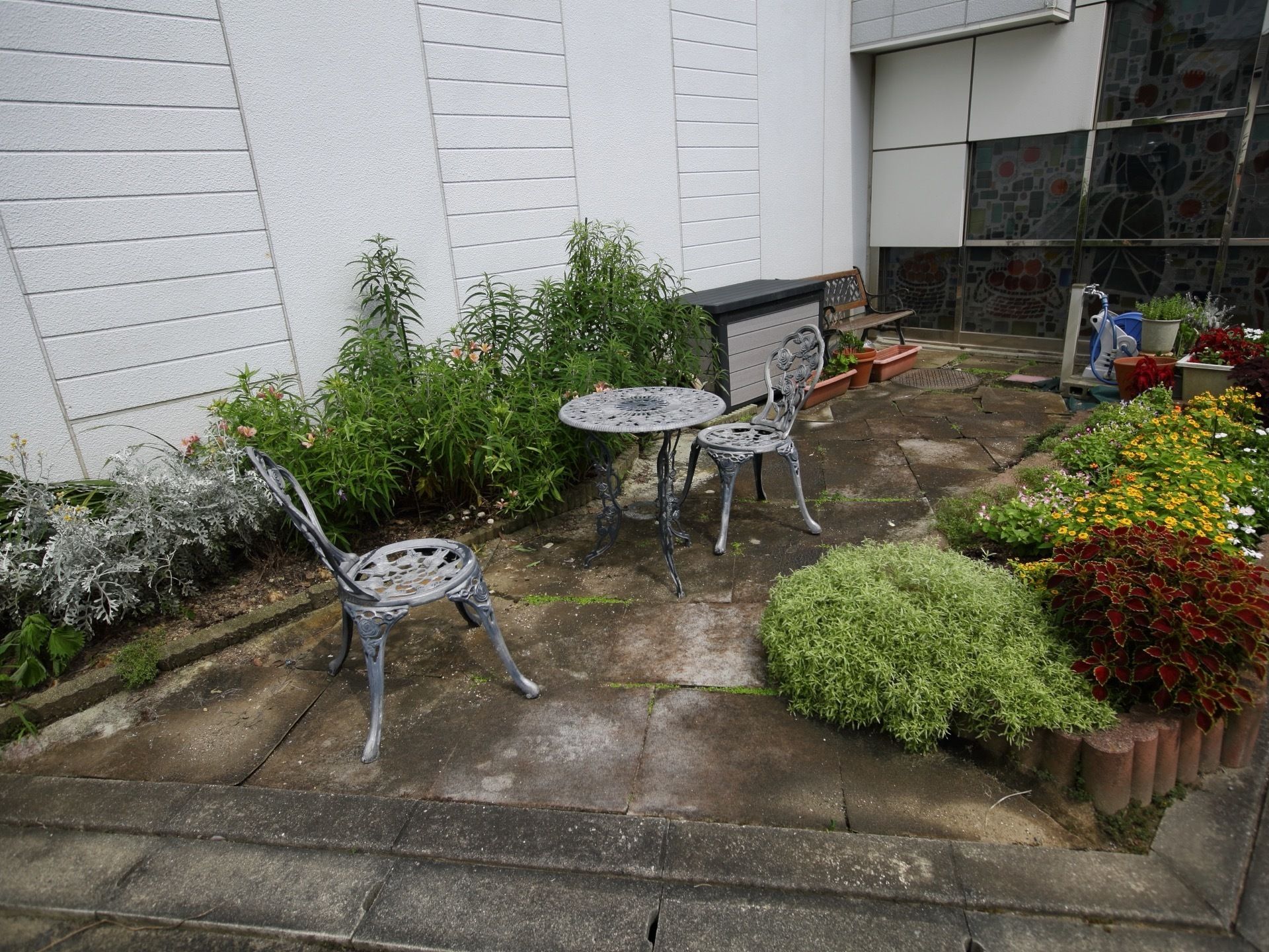 フラットな石畳に季節の花々が植えられた植え込みが備えてある。そばにはデザイン性のあるテーブルと椅子が配置されている。