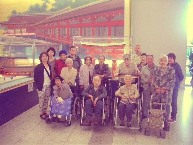 観光名所へ出かけた際の集合写真。介護度の異なる入居者がスタッフやほかの入居者の助けを借りながら同じように外出している。