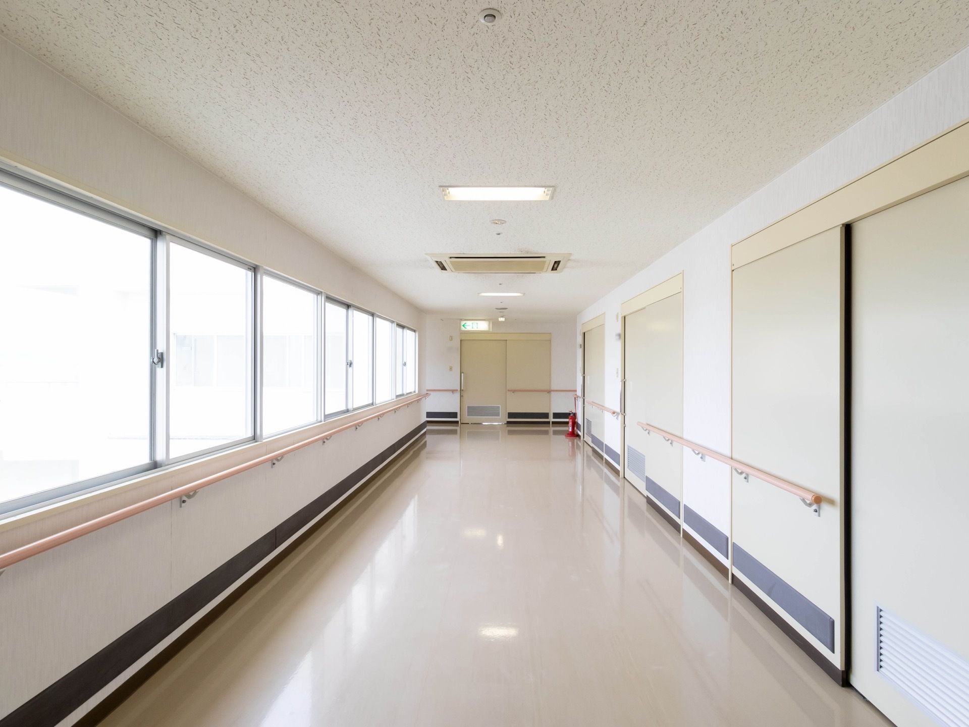 居室前の廊下で、白を基調とした明るい空間になっている。両サイドの壁には手すりが設置されており、奥に消火器が置かれている。