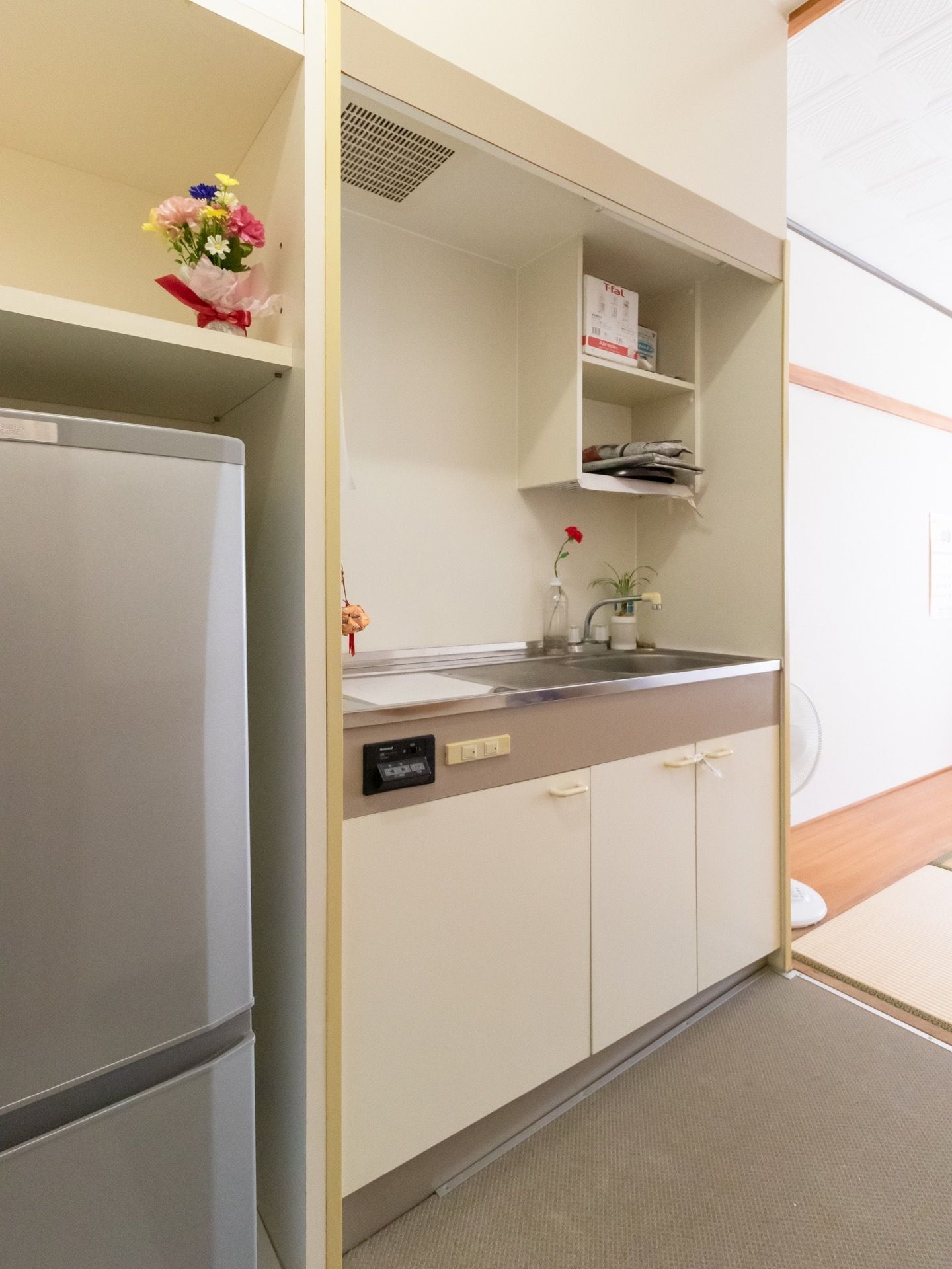 部屋にキッチンが備え付けられており、上下に収納スペースが確保されている。横には冷蔵庫が置かれている。