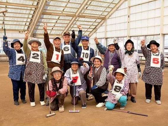 手を挙げて笑顔で撮影に応じる入居者の姿。グランドゴルフ場にて。
