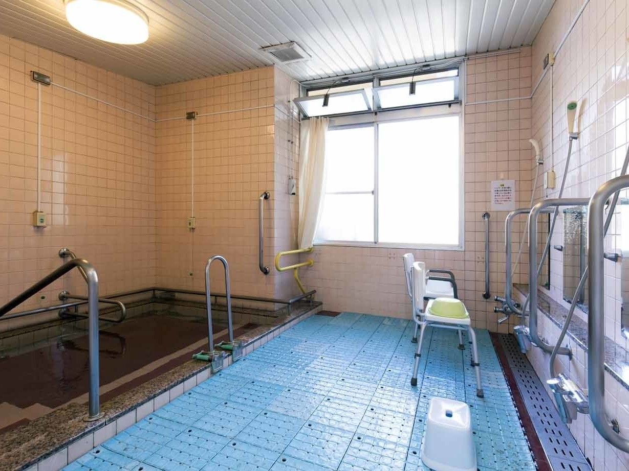ピンクのタイルをあしらった浴室。左手には大きな浴槽、右手にはシャワーとシャワーチェアある。
