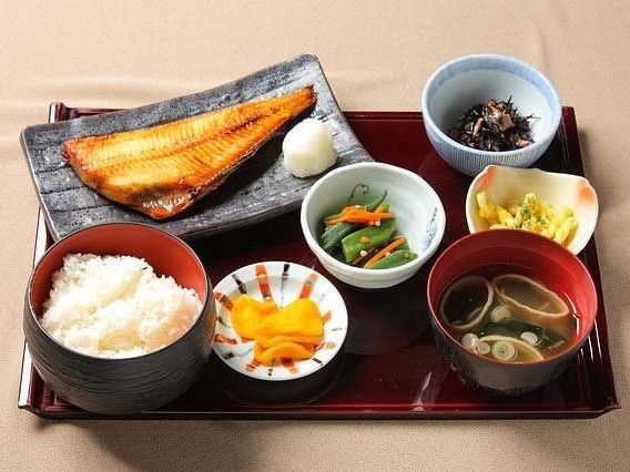 白いご飯とみそ汁が手前に置かれ、右奥にひじき、左奥にメイン料理の魚の干物、間に小鉢が数点がある。