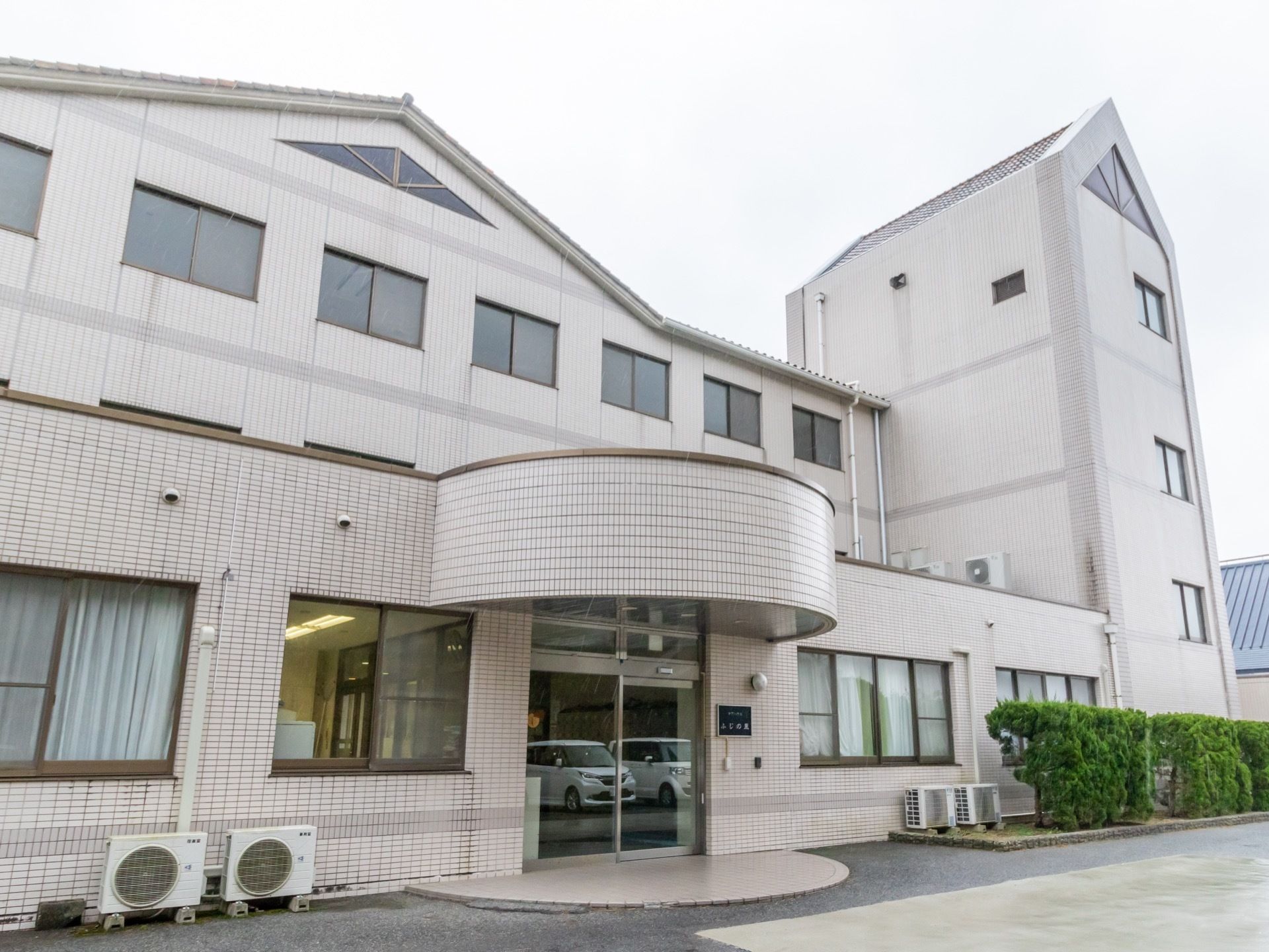 施設は３階建ての大きな建物で、１階に入口がある。入口近くの外壁には施設の種類と施設名を記したプレートが掲げられている。