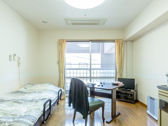 ミニキッチン付きの居室。キッチンには調理器具が置かれ、奥のリビングスペースでは2名の女性がティータイムを楽しんでいる。