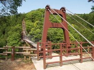 緑豊かな環境の中にあるつり橋。細長い釣り針の入り口には茶色い柵がある。