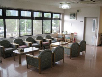 大きな窓が付いたロビーには応接セットが複数置かれていて奥にはテーブルセットがある。