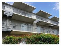 芝生が敷かれた庭が付いた3階建ての建物。庭には木も植えられていて、建物にはベランダも付いている。