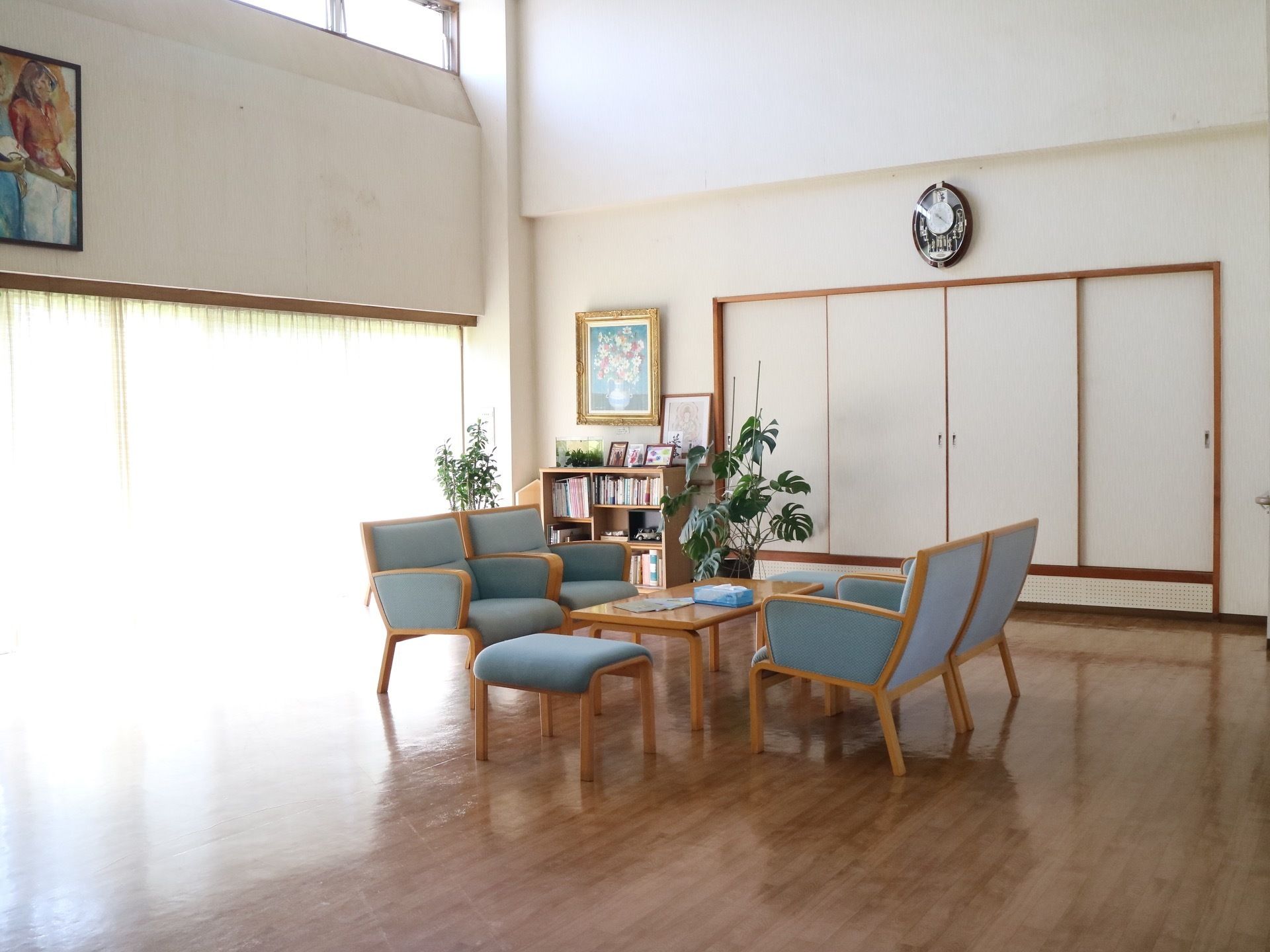 壁一面の窓からの採光で明るい休憩スペースがある。薄い青色の座面や背もたれがついたソファチェアが置かれている。
