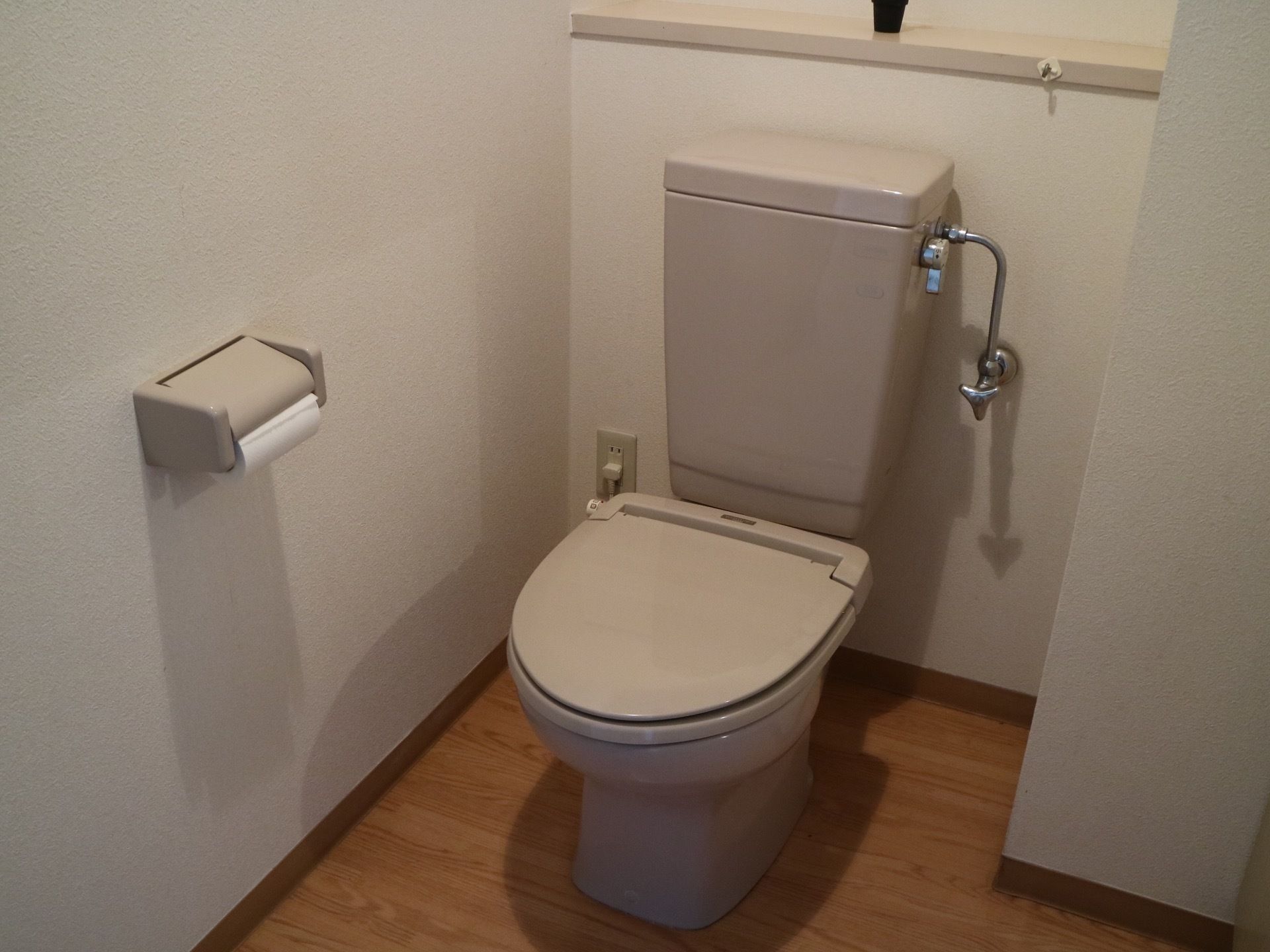 トイレは、落ち着いた色調のふたつきの便座である。壁にトイレットペーパーホルダーが一つ取り付けられている。