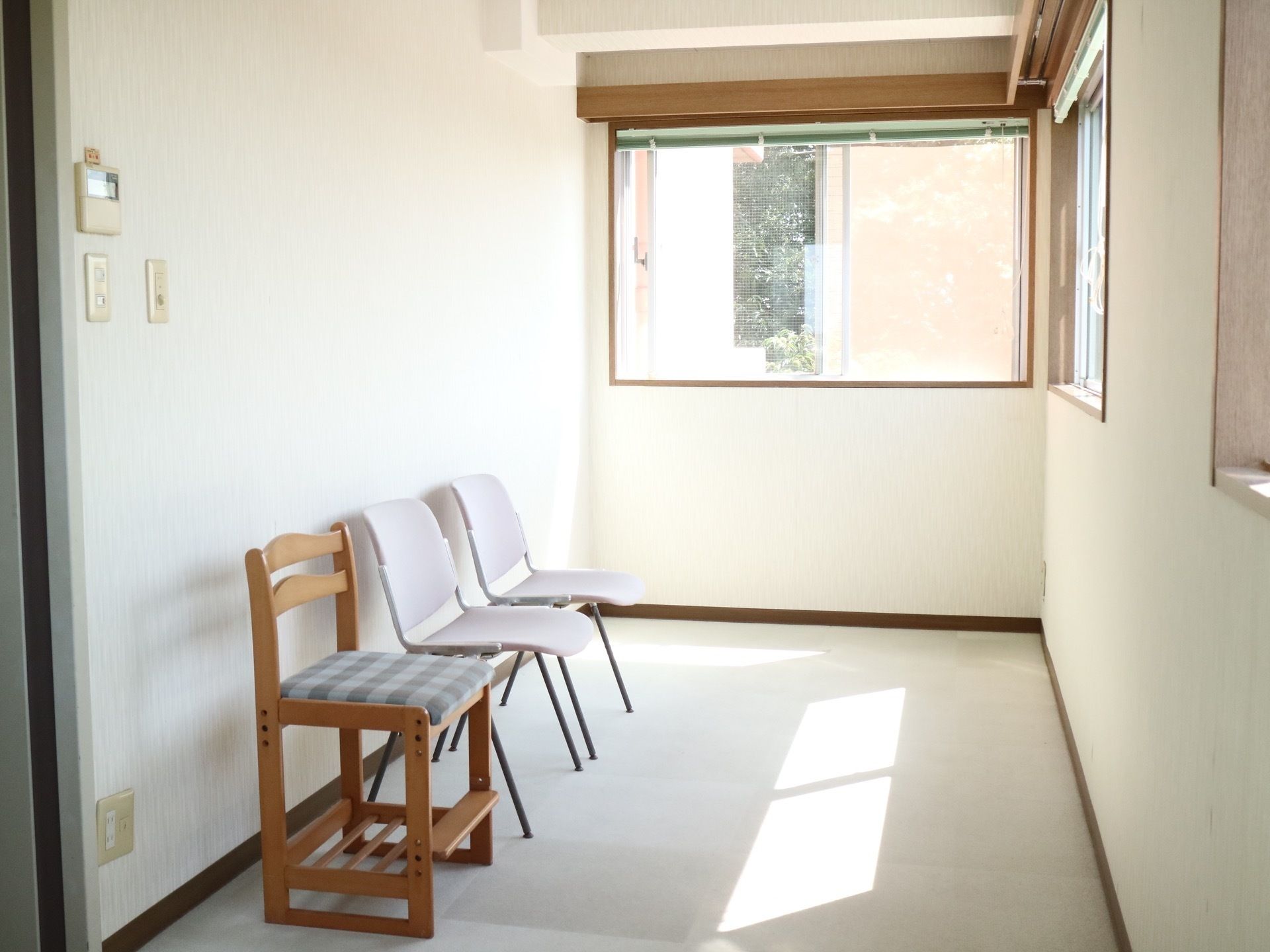 廊下のつきあたりに椅子が３脚置かれた休憩スペースがある。空調の操作パネルが壁に設置されている。窓から日差しが差し込んでいる。