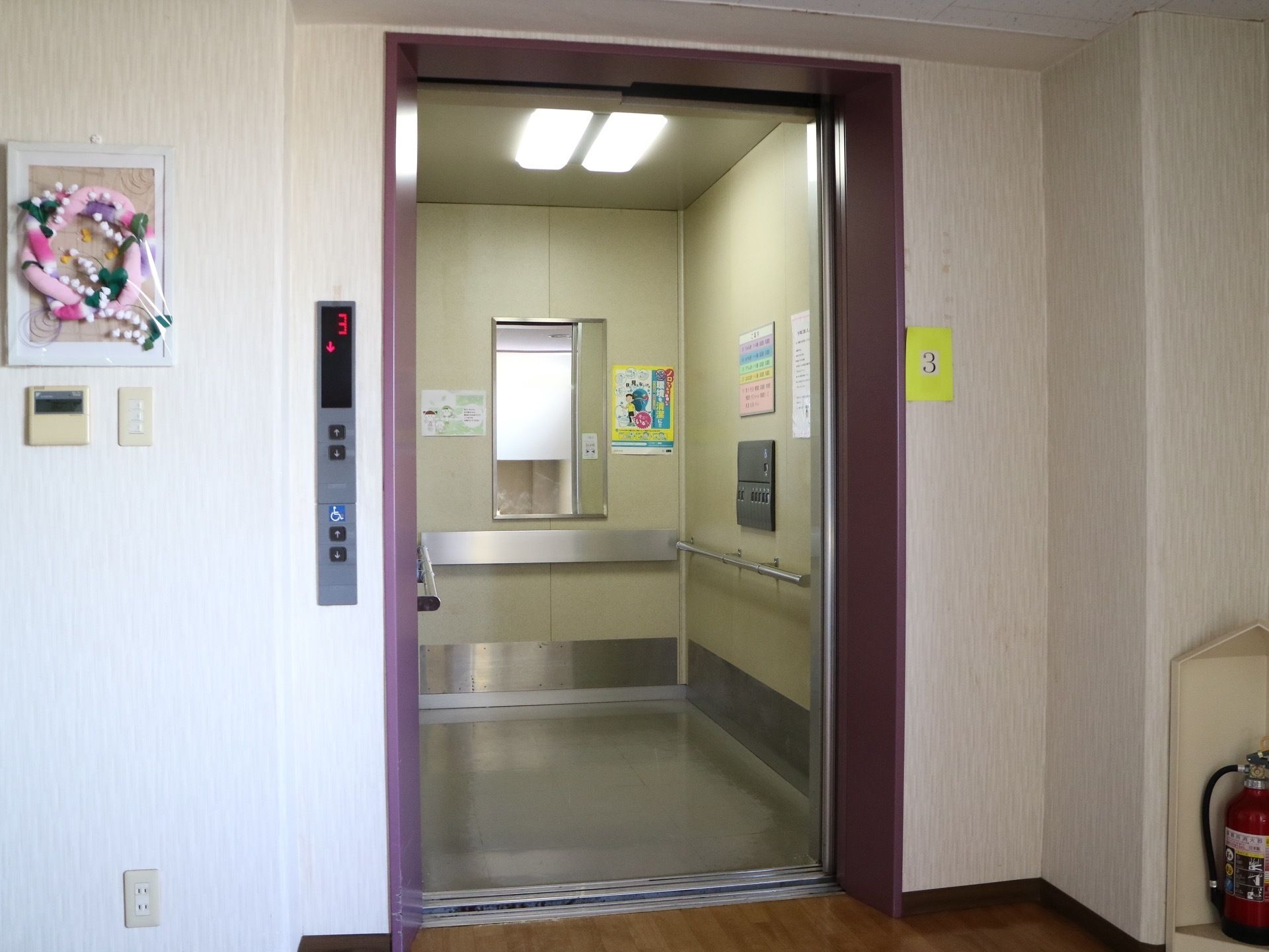 エレベーターがある。内部の正面には鏡があり、両側の壁には手すりがかかっている。乗降口のすぐそばに階数表示がある。