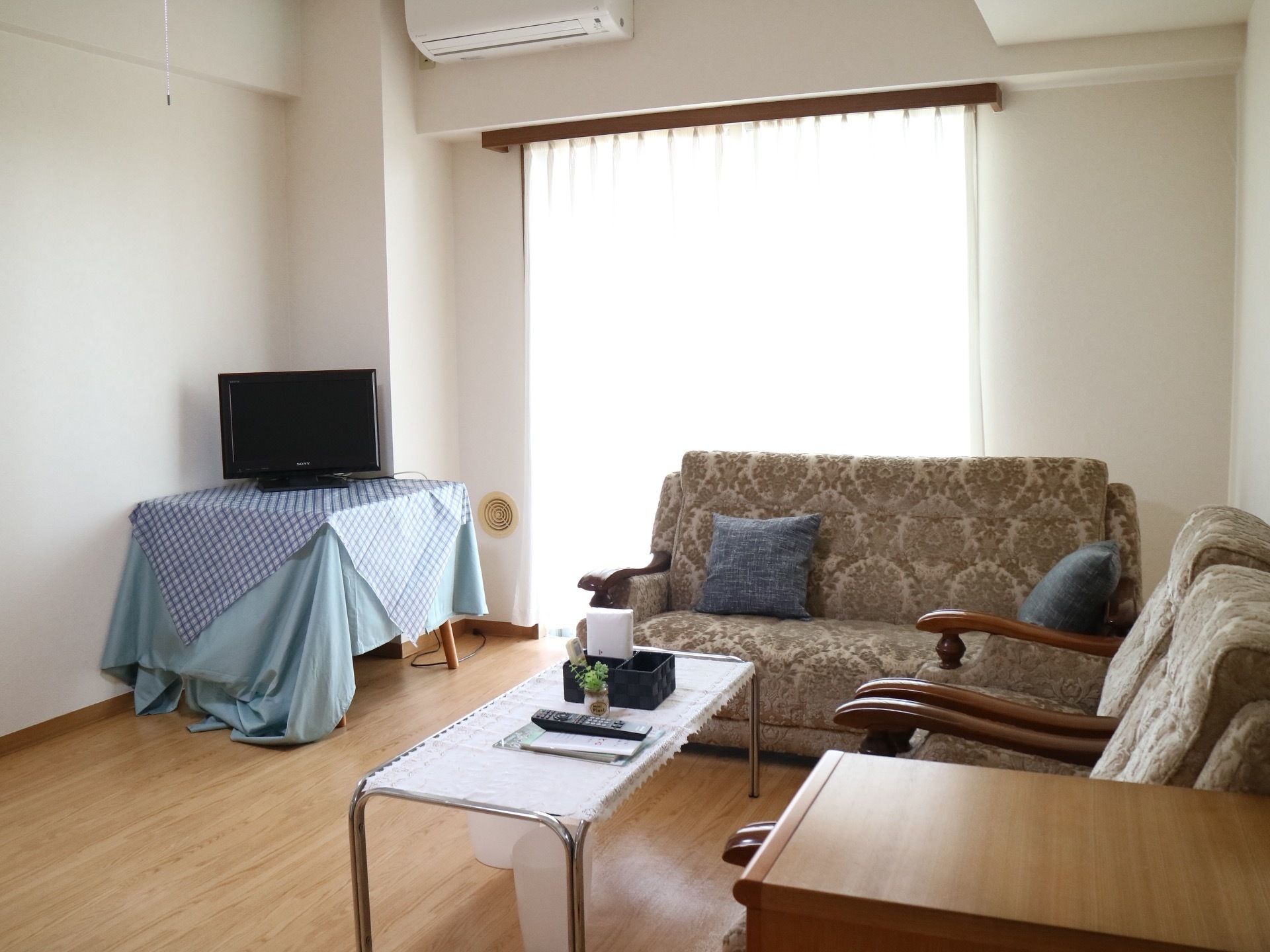 居室に、２人掛けのソファ１台と１人掛けのソファ２台が、ローテーブルを囲むようにして置かれている。台の上にテレビが載っている。