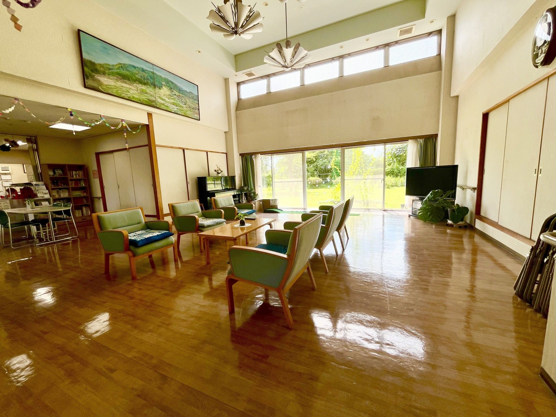 壁一面の窓からの採光で明るい休憩スペースがある。薄い青色の座面や背もたれがついたソファチェアが置かれている。