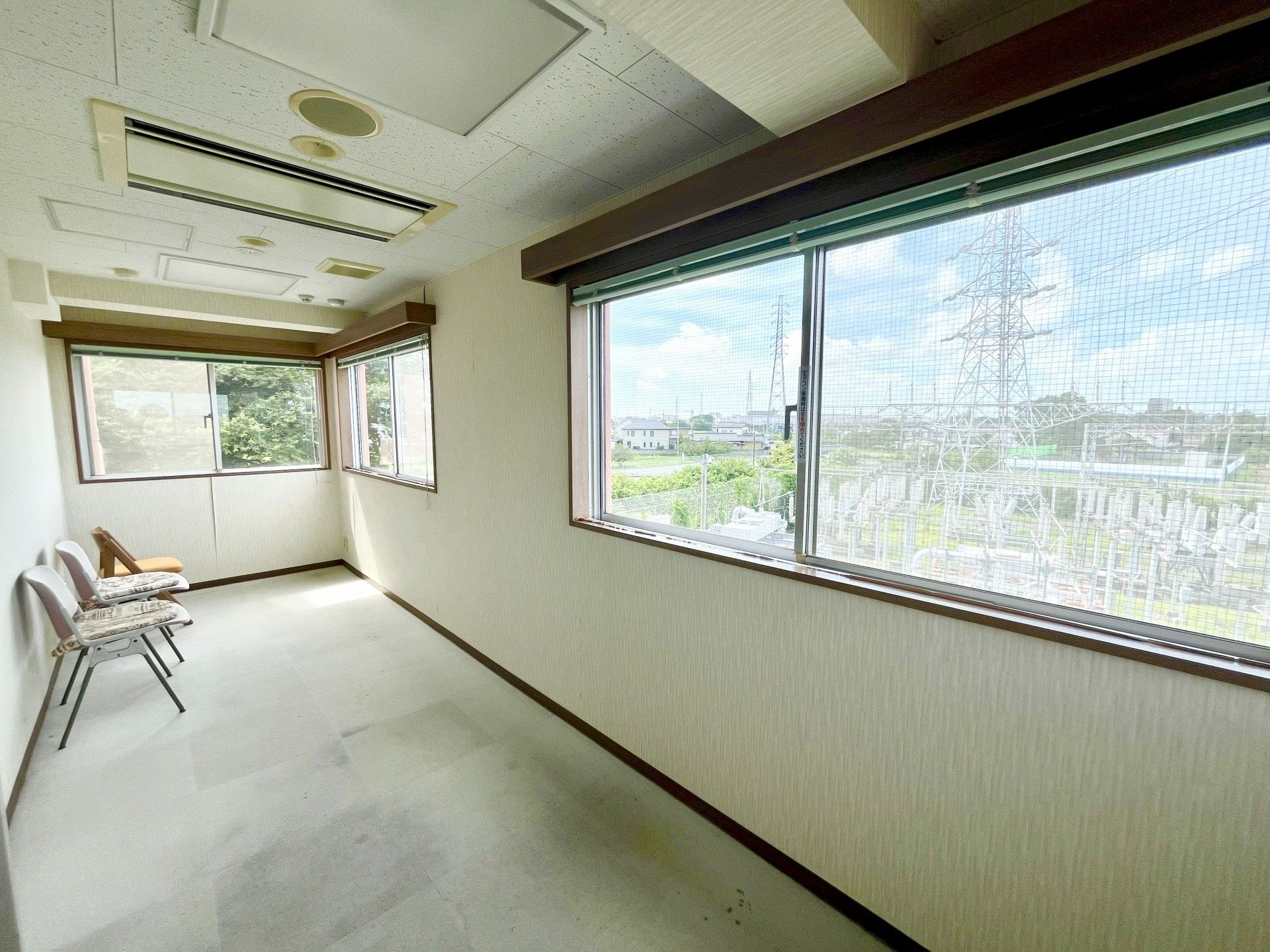 廊下のつきあたりに椅子が３脚置かれた休憩スペースがある。空調の操作パネルが壁に設置されている。窓から日差しが差し込んでいる。