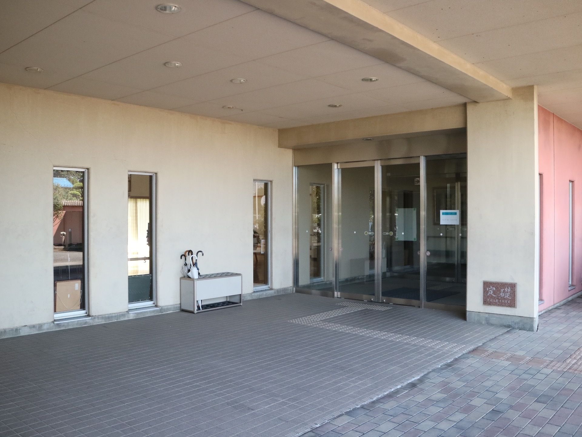 玄関前は屋根がある構造になっていて、その天井には埋め込み式の照明がいくつも設置されている。傘立てに傘が置かれている。