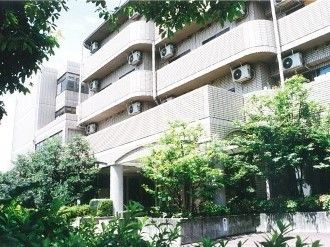 各フロアにベランダが付いた白っぽい建物の周辺にはたくさんの緑が植えられている。