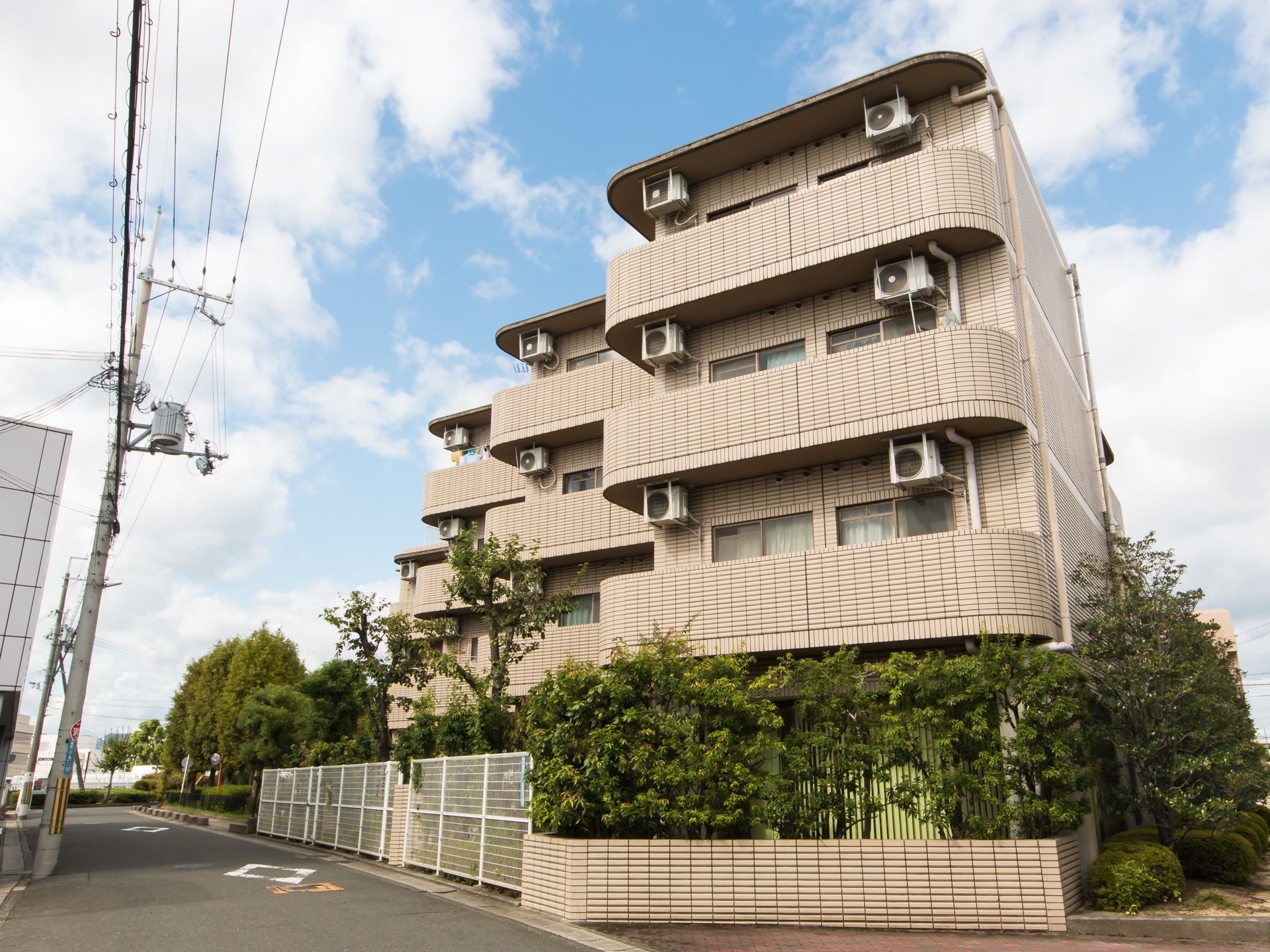 道路に面して建っている地上４階建てのタイル張りの施設である。建物の周囲や奧の敷地に草木が茂っている。