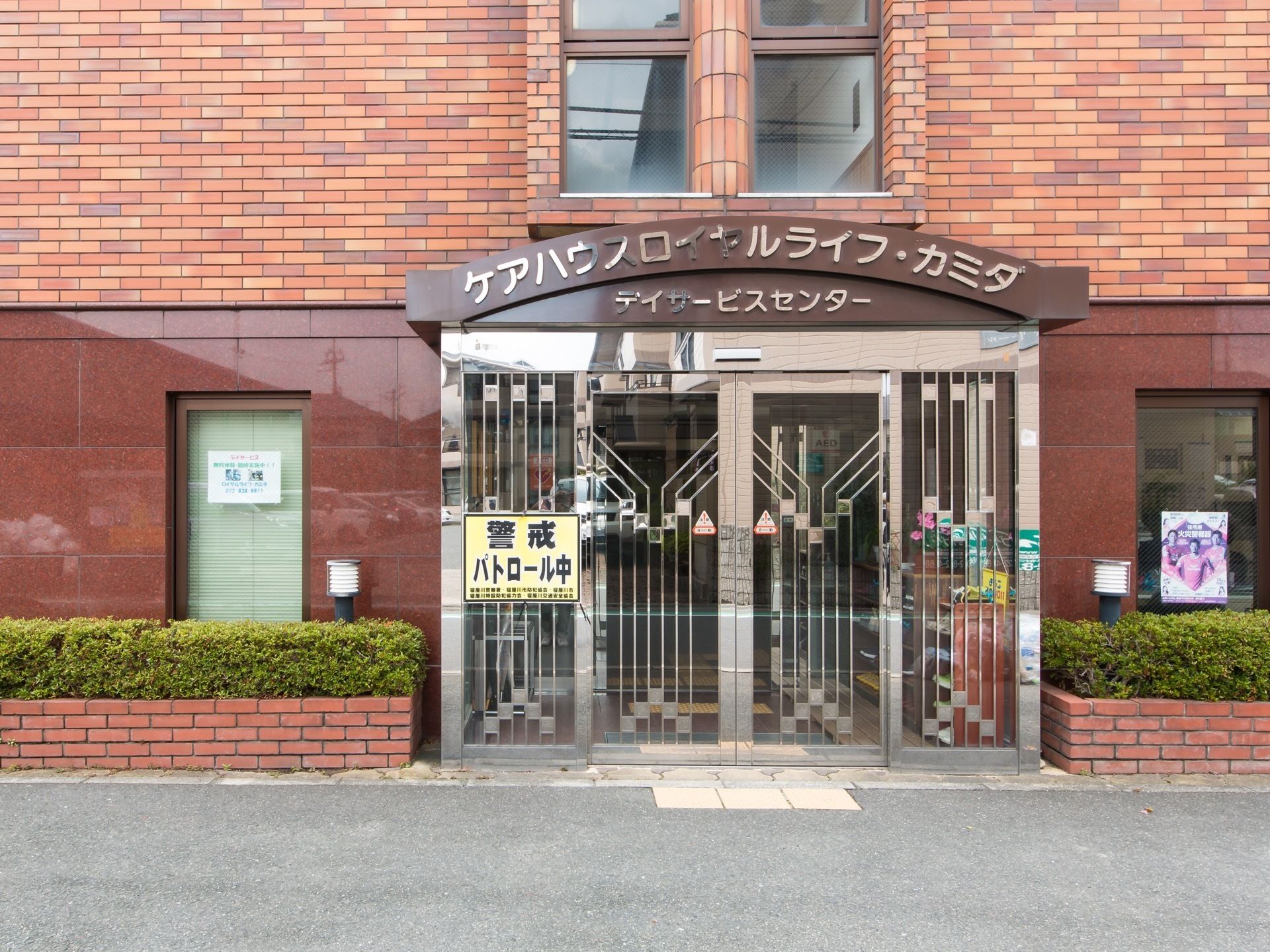 レンガ風の外壁の建物である。模様の入ったステンレス製のガラス戸の玄関ドアが設置されている。玄関の左側に、黄色い貼り紙がある。