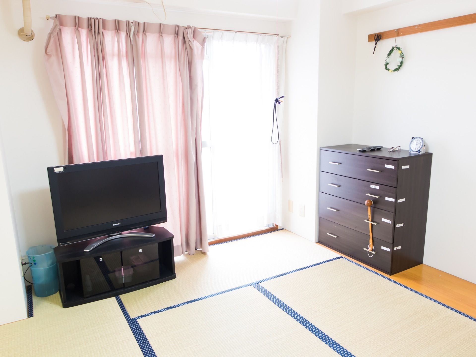 和室の部屋の窓に、ピンク色のカーテンが取り付けられている。引き出し式の収納家具と液晶テレビが置いてある。