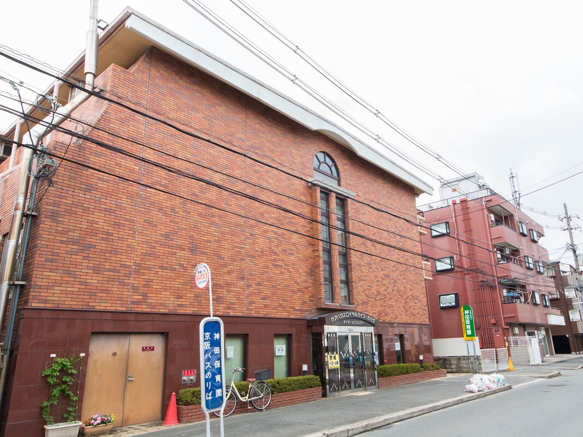 公道沿いに地上4階建てのレンガ調の施設が建っている。広い歩道があり、ゴミ収集所やバス停が設けられている。