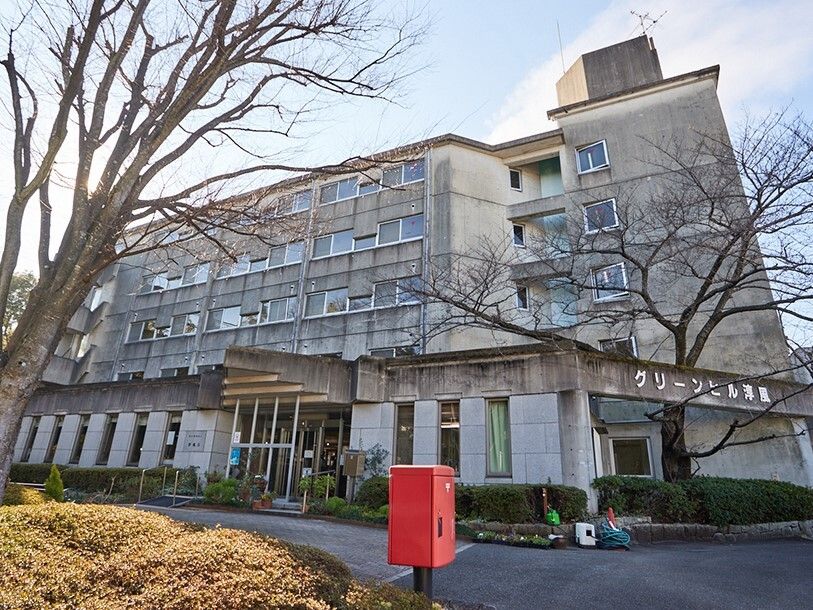 赤いポストの後ろにはグレーの外壁の大きな建物があり、建物の周りは草木が植えられている。