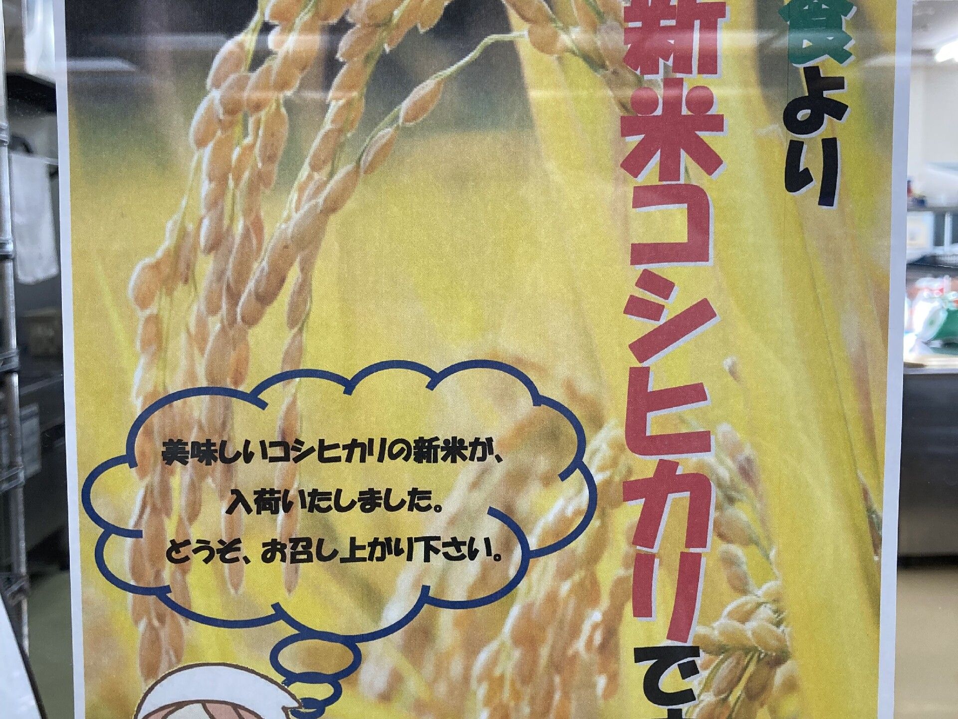 「新米コシヒカリです」と書かれた稲穂のポスターが飾られている。後ろに厨房がある。