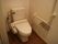 白い壁の間に設置されているトイレである。壁には、Ｌ字型に手すりが取り付けられ、ペーパーホルダーが２つある。